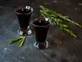 Dwa kieliszki ciemnego, aromatycznego nalewki z czernic, ozdobione gałązkami rozmarynu.