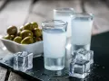 Trzy kieliszki ouzo z lodem i miseczka oliwek na drewnianym tle.