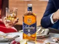 Elegancka butelka Ballantine's 10 Years Old na stole, obok kieliszka z bursztynowym płynem. To nie bourbon, lecz szkocka whisky, idealna na specjalne okazje.