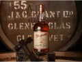 Glenfarclas 10YO, idealny wybór do rankingu top 10 whisky. Butelka na tle beczki z destylarni.