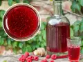 Butelka i kieliszek wypełnione rubinową nalewką z malin, obok świeże owoce i korek.
