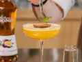 Barman dekoruje drink likierem z marakui, dodając listek mięty. Obok stoi butelka Monin.
