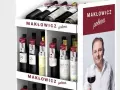 Regał z butelkami wina, z etykietami "Makłowicz poleca" i zdjęciem Roberta Makłowicza.