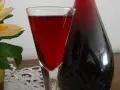 Szklanka z nalewką z aronii mrożonej na wódce, obok ciemna butelka. W tle ozdobny kwiat.
