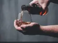 Dłoń nalewa bursztynowy płyn z butelki do szklanki. Czy whisky to bimber?