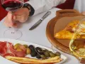 Ręka trzyma kieliszek czerwonego wina wytrawnego. Obok talerz z wędliną, oliwkami i grissini oraz chaczapuri i kieliszek białego wina.