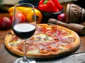 Idealne wino do pizzy, z kieliszkiem czerwonego wina i składnikami na pizze w tle.