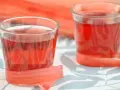 Dwa kieliszki z rubinową nalewką z rabarbaru, ozdobione łodygami tej rośliny.