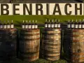 Butelki whisky Benriach stoją na beczkach, które czekają na dojrzewanie w pomieszczeniu.