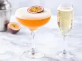 Pomarańczowy drink z pianką i marakują, obok kieliszek szampana. Idealny white lady drink na letnie popołudnie.
