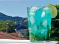 Orzeźwiający drink z blue curacao i sprite, z miętą i lodem, ozdobiony plasterkiem limonki, na tle zielonych wzgórz.