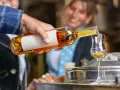 Mężczyzna nalewa złocisty grappa alkohol do kieliszka. W tle uśmiechnięta kobieta.