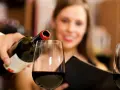 Kelner nalewa wino, a uśmiechnięta kobieta czeka na kieliszek. Wino zawiera siarczyny, które pomagają w jego konserwacji.