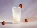 Orzeźwiający drink z liczi, ozdobiony owocem, z dwoma całymi liczi obok. Idealny na letnie popołudnie.