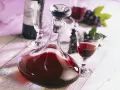 Kryształowa karafka wypełniona rubinową nalewką z winogron na spirytusie, obok kieliszek i kiść ciemnych winogron.