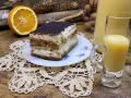 Słodki deser tiramisu, połówka pomarańczy i kieliszek likieru ze skórek pomarańczy na drewnianym blacie.