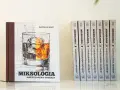 Książka "Miksologia Amerykańska Whiskey" Patryka Le Narta, z ilustracją szklanki z lodem i bursztynowym trunkiem. Obok niej rząd identycznych tomów.