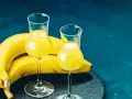 Dwa kieliszki z żółtym likierem bananowym obok dojrzałych bananów. Idealny przepis na domowy likier bananowy.