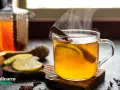 Rozgrzewająca herbata z whisky, z plastrem cytryny i laską cynamonu, paruje w szklance. Obok leżą cytryny i przyprawy.