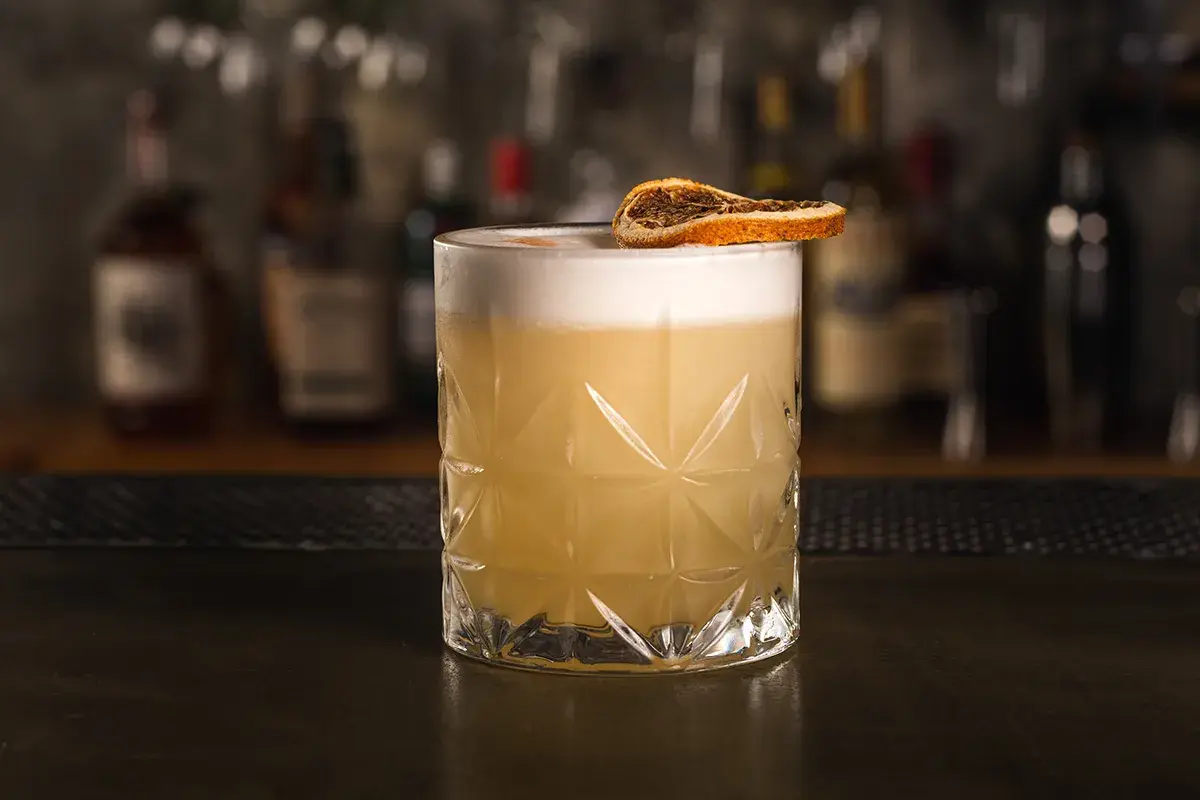 Klasyczny whisky sour z pianką i plasterkiem suszonej pomarańczy, gotowy do degustacji.