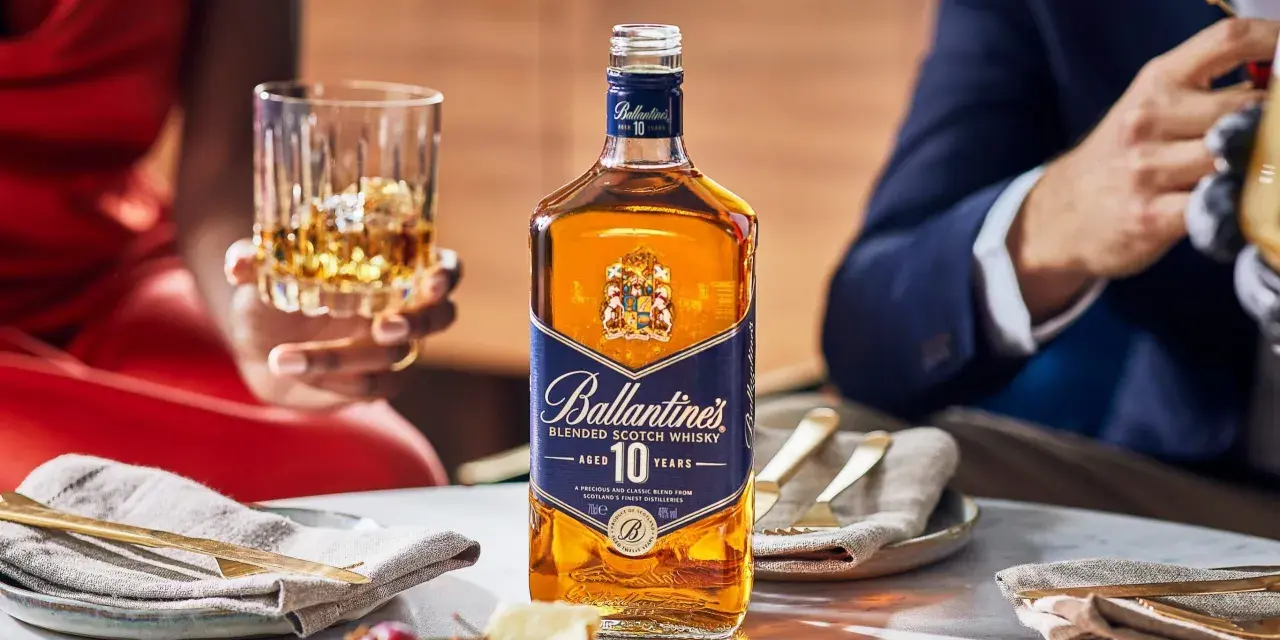 Elegancka butelka Ballantine's 10 Years Old na stole, obok kieliszka z bursztynowym płynem. To nie bourbon, lecz szkocka whisky, idealna na specjalne okazje.