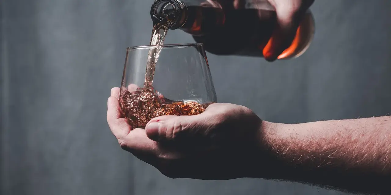 Dłoń nalewa bursztynowy płyn z butelki do szklanki. Czy whisky to bimber?
