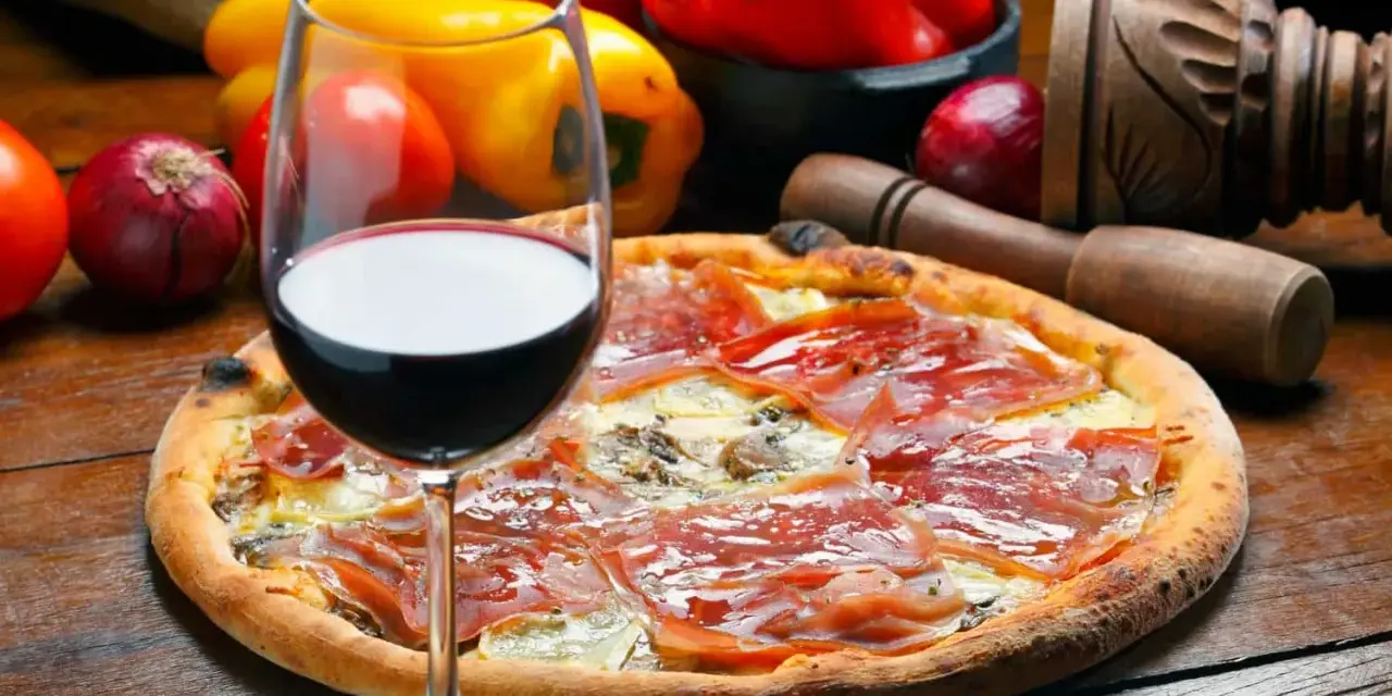 Idealne wino do pizzy, z kieliszkiem czerwonego wina i składnikami na pizze w tle.