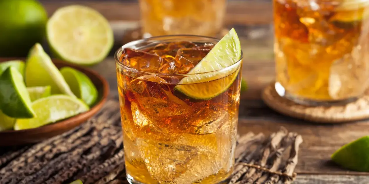 Orzeźwiający drink z whisky i coca colą, ozdobiony plasterkiem limonki. Obok miseczka z kawałkami limonki.