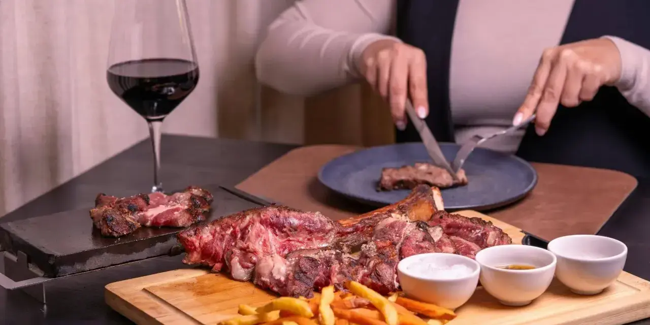 Idealne **jakie wino do wieprzowiny**? Czerwone wino i soczysta wieprzowina na desce, z frytkami i sosami.