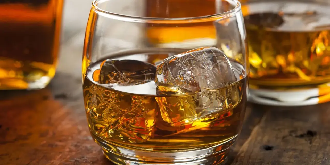 Szklanka złocistego trunku z lodem, obok butelki. Dylemat: whisky szkocka czy irlandzka?