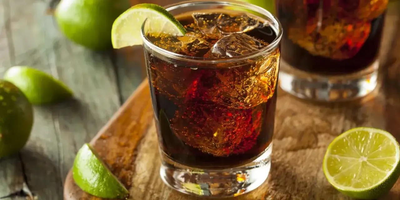 Orzeźwiający drink: bacardi z czymś ciemnym i lodem, ozdobiony plasterkami limonki.