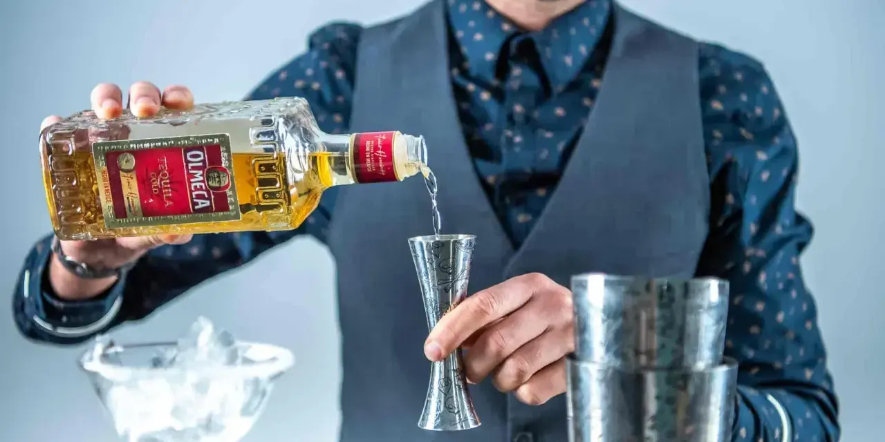 Barman nalewa Olmeca Tequila Gold do jiggera, idealna tequila do margarity. Obok kieliszek z lodem i shaker.
