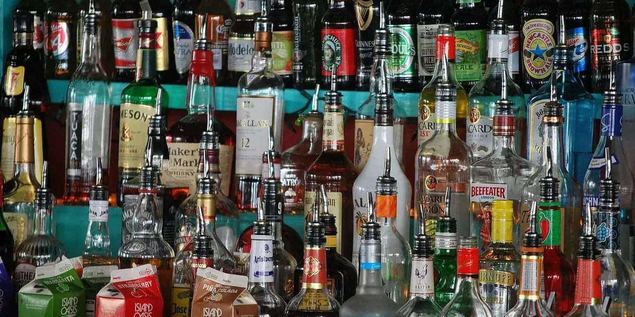 Różnorodne butelki alkoholi, w tym whisky, stoją na półce. Wskazówki, jak przechowywać whisky, mogą być przydatne przy tak bogatym asortymencie.