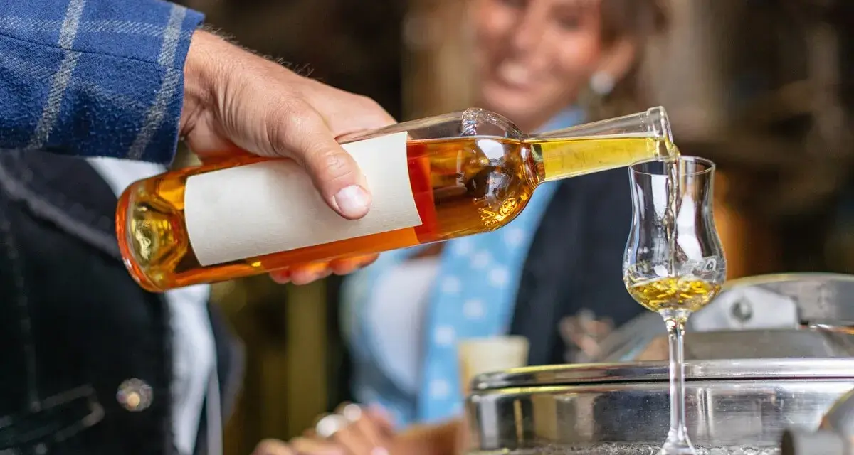 Mężczyzna nalewa złocisty grappa alkohol do kieliszka. W tle uśmiechnięta kobieta.