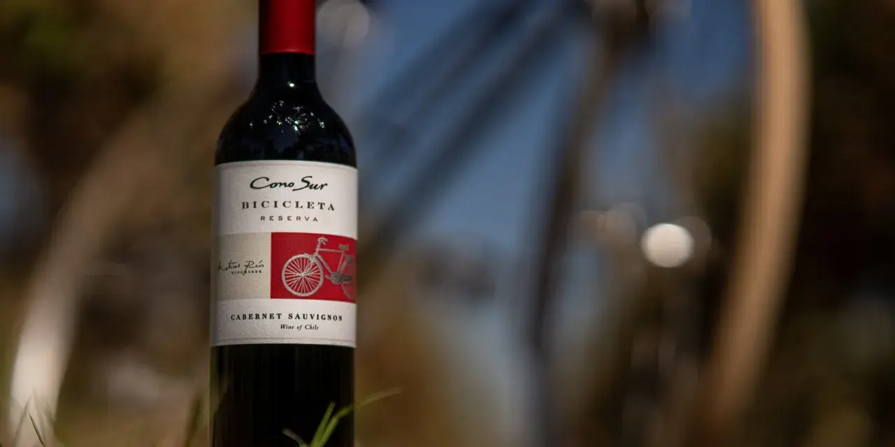 Butelka wina Cabernet Sauvignon z rowerem na etykiecie, stojąca na trawie.