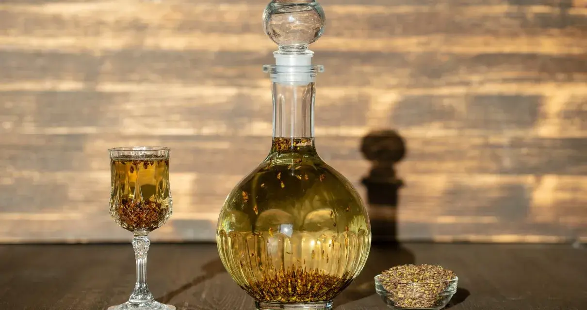 Wódka z pieprzem przepis: nalewka w karafce i kieliszku, obok miseczka z ziarnami pieprzu.