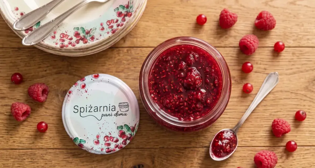 Słoik domowej nalewki z malin, przepis babci. Obok świeże maliny i czerwone porzeczki, talerze z owocowym wzorem.