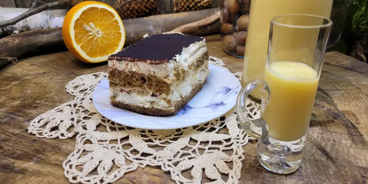Słodki deser tiramisu, połówka pomarańczy i kieliszek likieru ze skórek pomarańczy na drewnianym blacie.