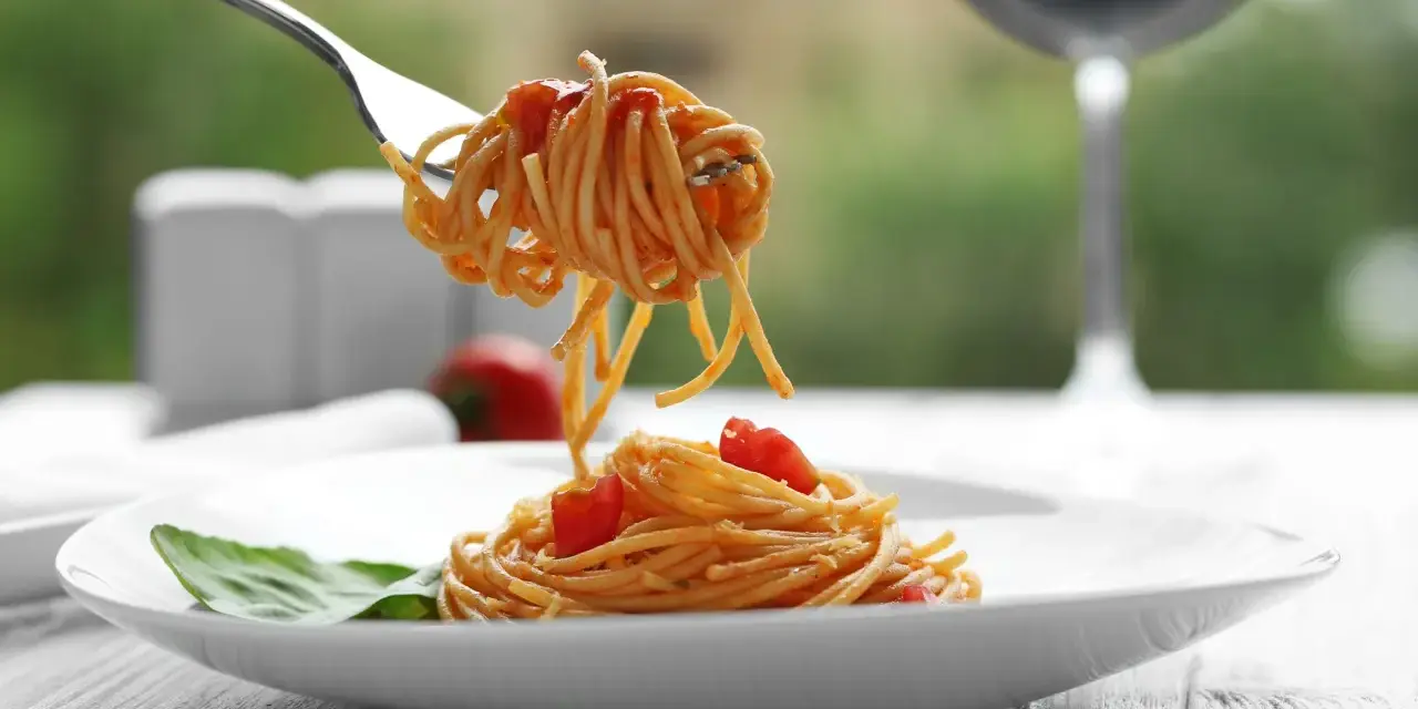 Widok na talerz spaghetti z sosem pomidorowym i listkiem bazylii. Widelec podnosi porcję makaronu. Idealne pytanie: jakie wino do bolognese?