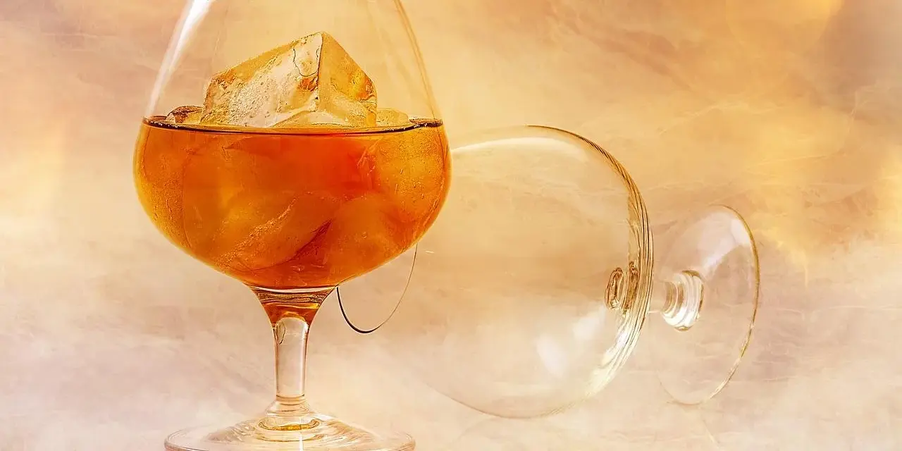 Kieliszek z bursztynowym płynem i lodem, obok pusty, przewrócony kieliszek. Idealny sposób, jak pić brandy.