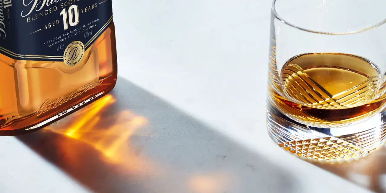 Butelka Ballantine's 10 Years Old i szklanka z bursztynowym płynem, przypominającym smak bourbona.