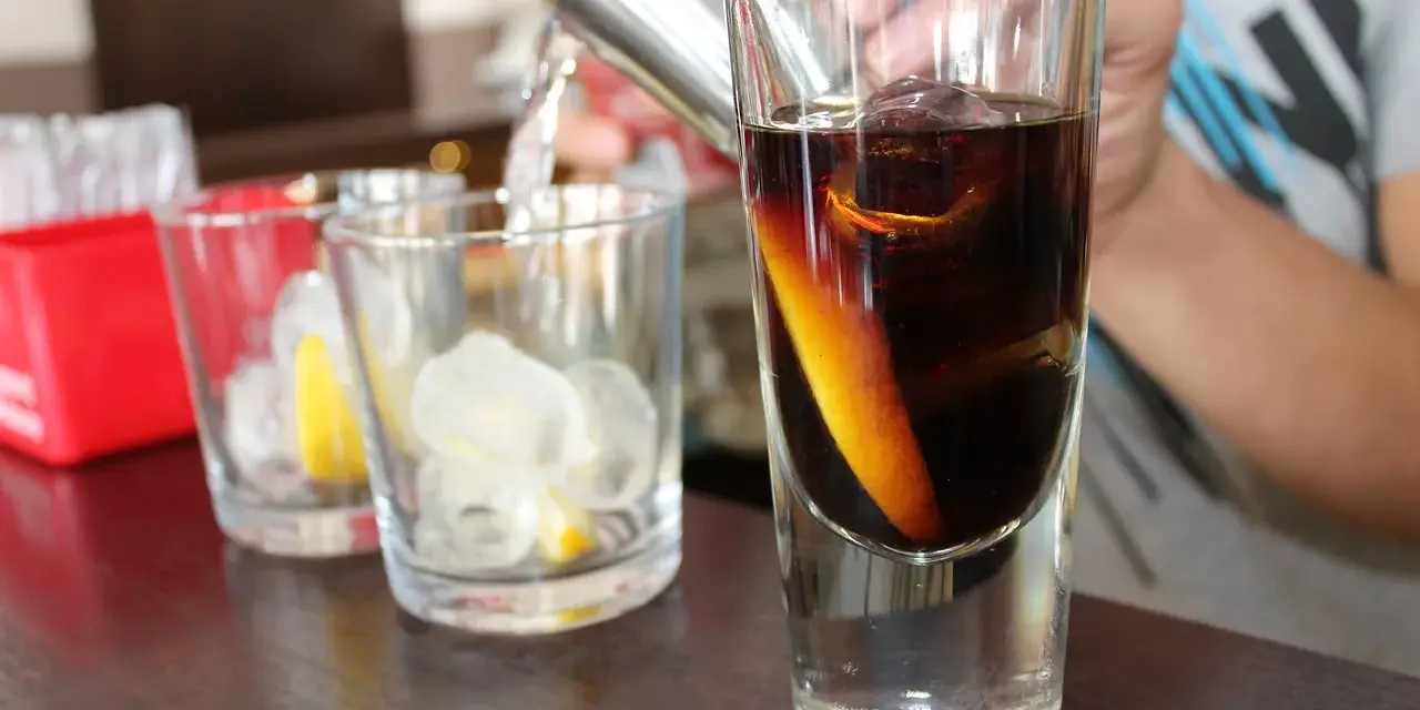 Elegancka porcja whisky z lodem i skórką pomarańczy, przygotowywana w szklance.