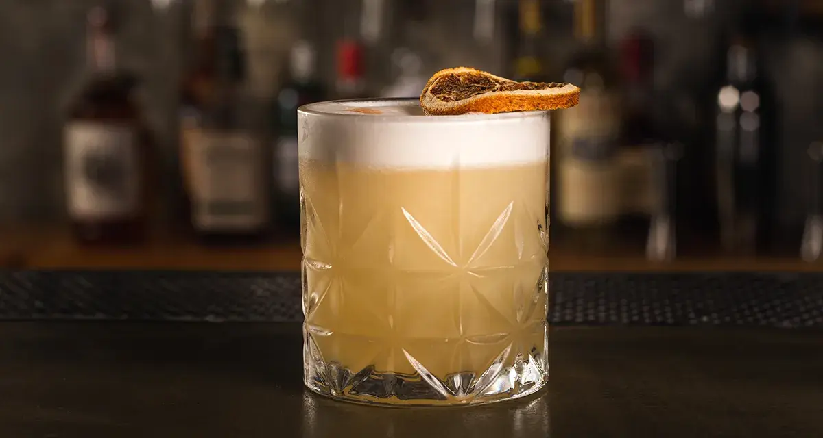 Klasyczny whisky sour z pianką i plasterkiem suszonej pomarańczy, gotowy do degustacji.