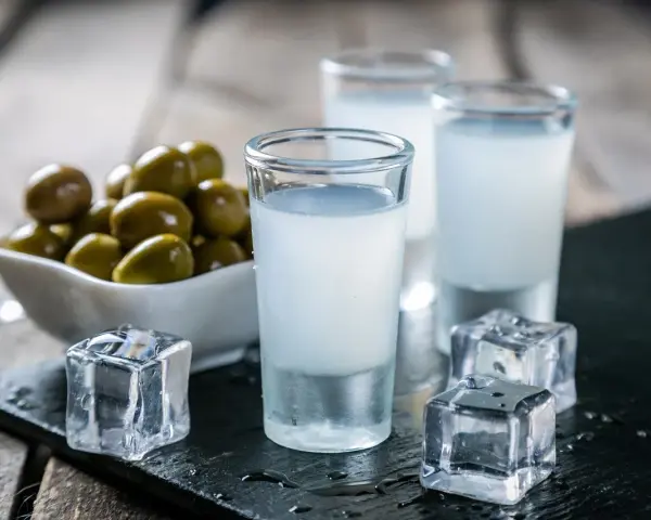 Trzy kieliszki ouzo z lodem i miseczka oliwek na drewnianym tle.