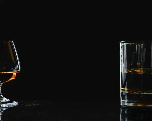 Kieliszek z brandy i szklanka z whisky na ciemnym tle.