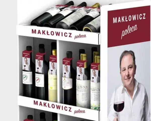 Regał z butelkami wina, z etykietami "Makłowicz poleca" i zdjęciem Roberta Makłowicza.