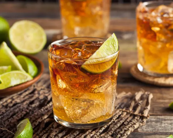 Orzeźwiający drink z whisky i coca colą, ozdobiony plasterkiem limonki. Obok miseczka z kawałkami limonki.