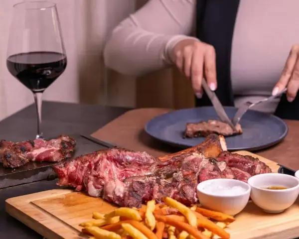 Idealne **jakie wino do wieprzowiny**? Czerwone wino i soczysta wieprzowina na desce, z frytkami i sosami.