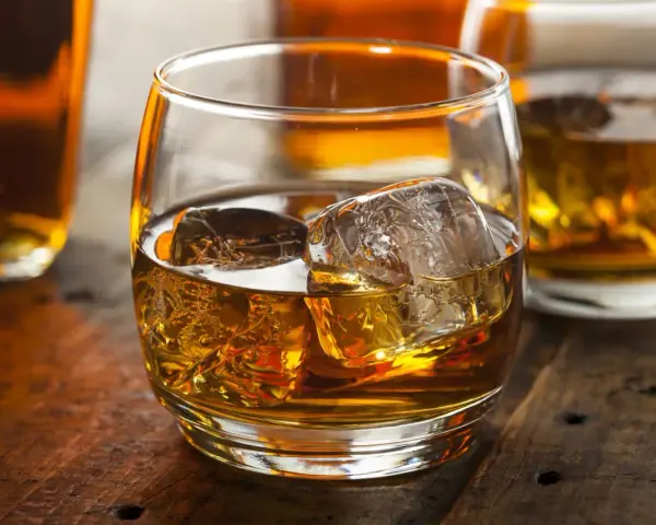 Szklanka złocistego trunku z lodem, obok butelki. Dylemat: whisky szkocka czy irlandzka?