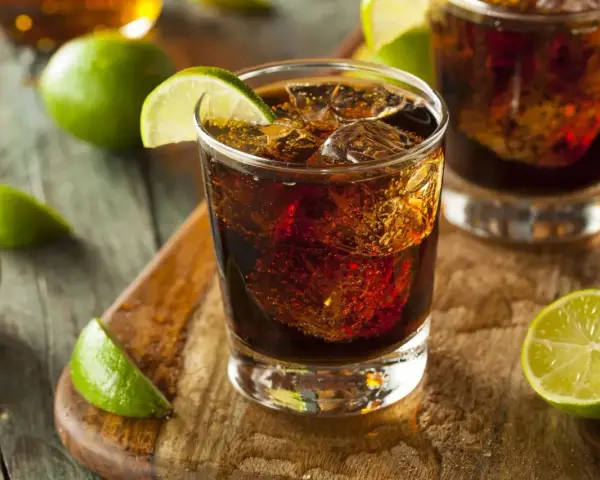 Orzeźwiający drink: bacardi z czymś ciemnym i lodem, ozdobiony plasterkami limonki.
